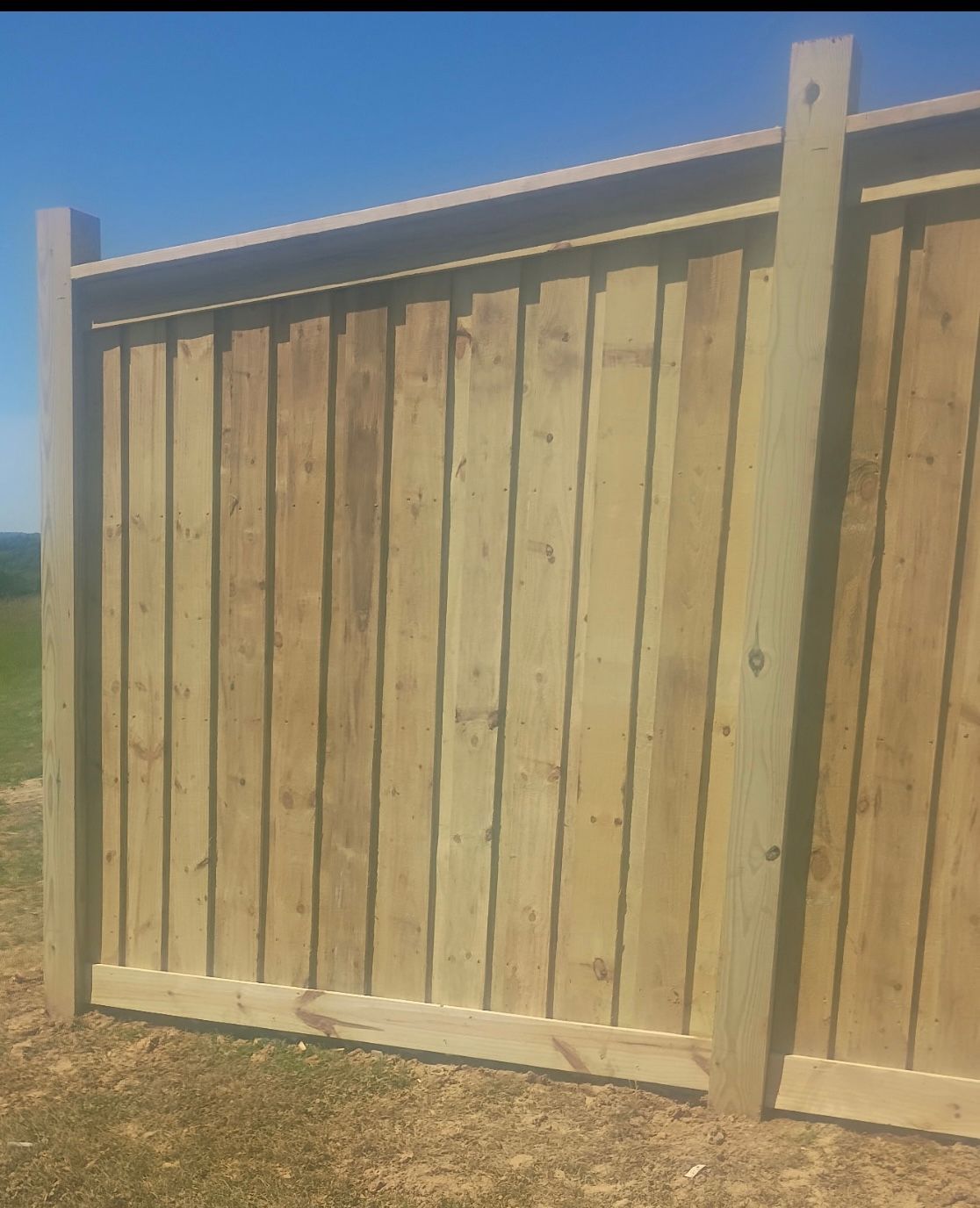 Wooden fence panel with vertical planks under a clear blue sky in a dry field