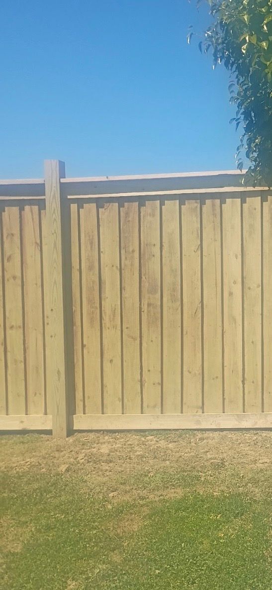 Wooden backyard fence under a clear blue sky, with grass in the foreground.