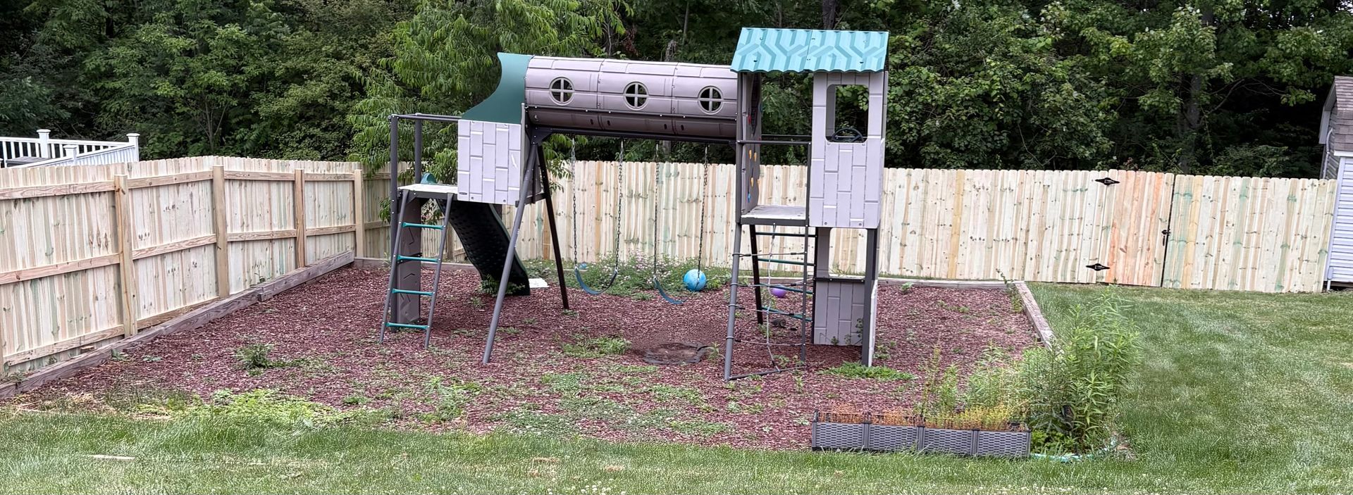 Backyard playset with a slide, climbing tunnel, and small roofed platforms on a grassy lawn.