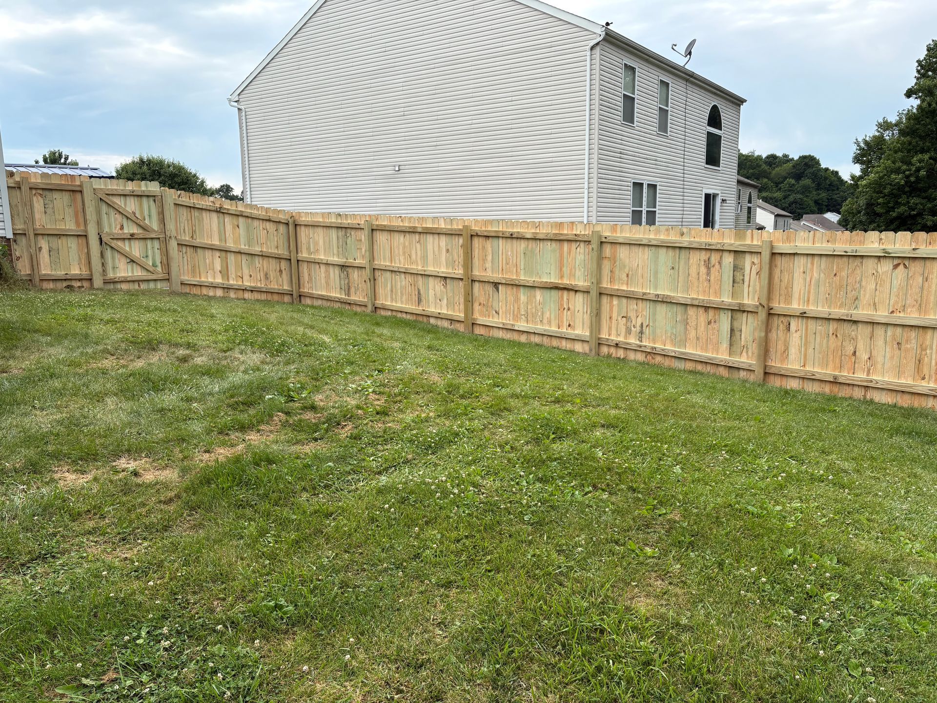 Grassy backyard with a wooden fence and a covered house in the background