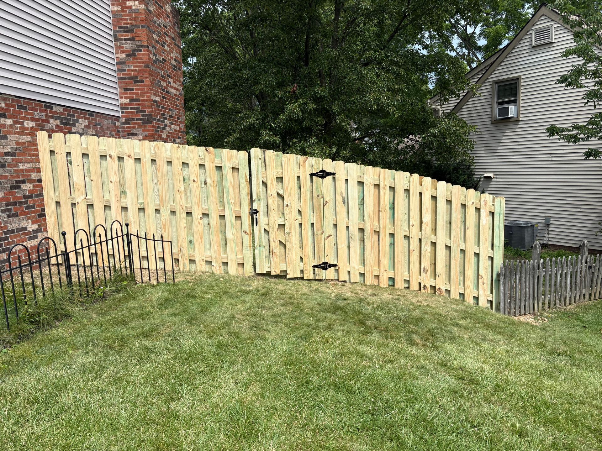 New wooden fence panels along a grassy yard beside a brick house and trees