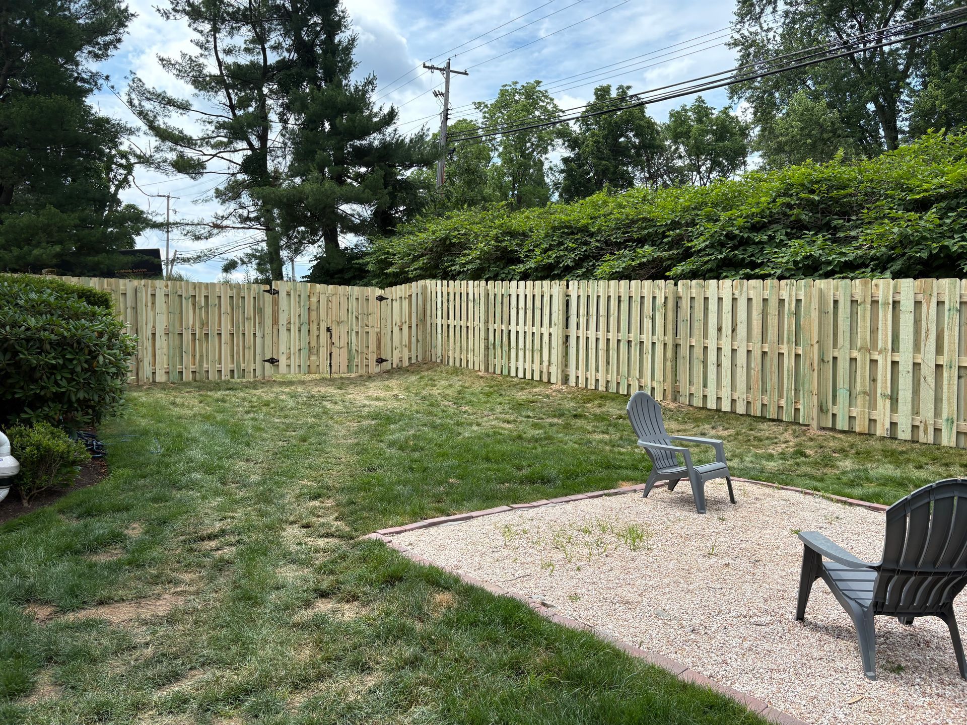 Backyard with wooden fence, grass, and a gravel patio with two outdoor chairs