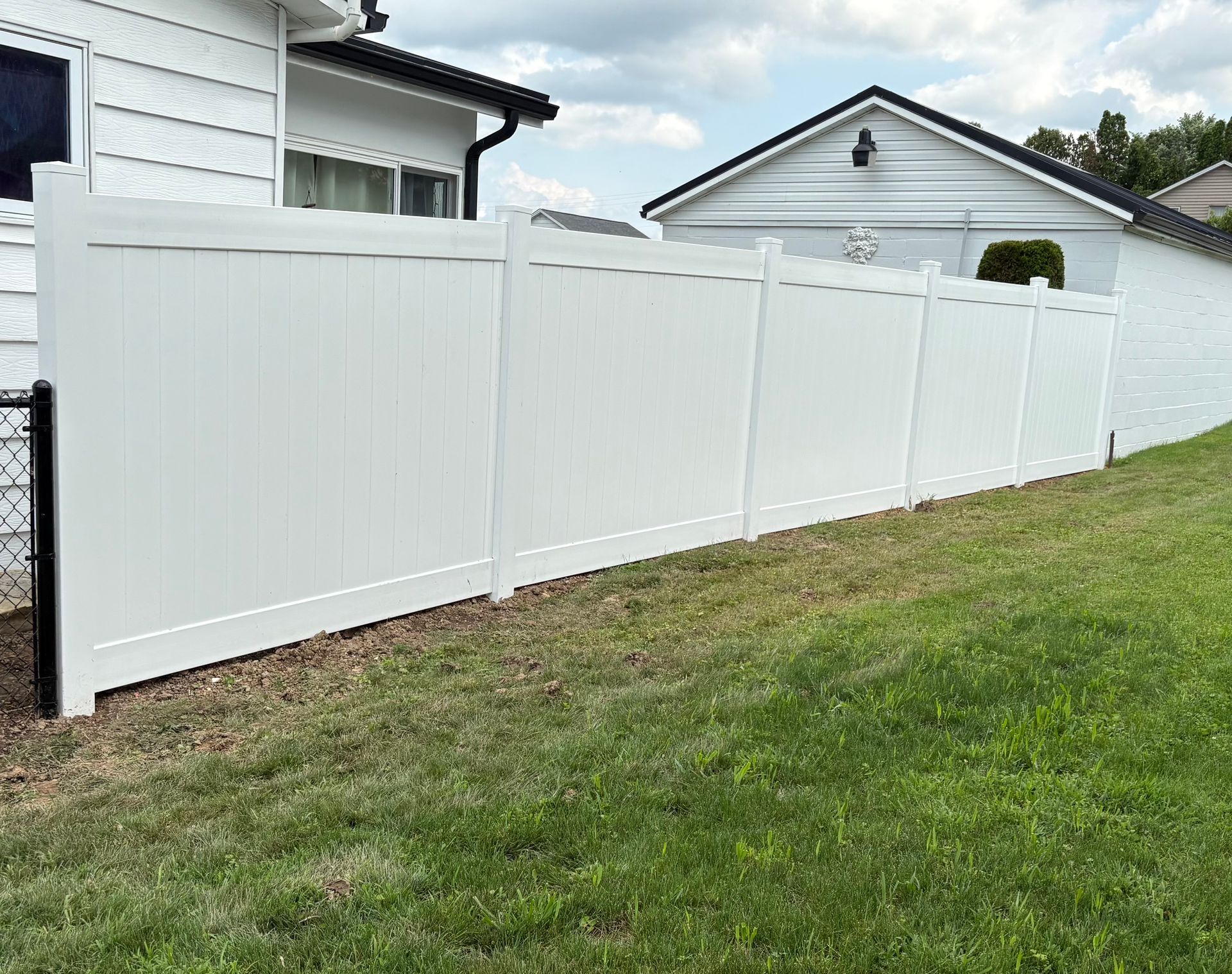 White vinyl privacy fence along a grassy backyard beside a light-colored house