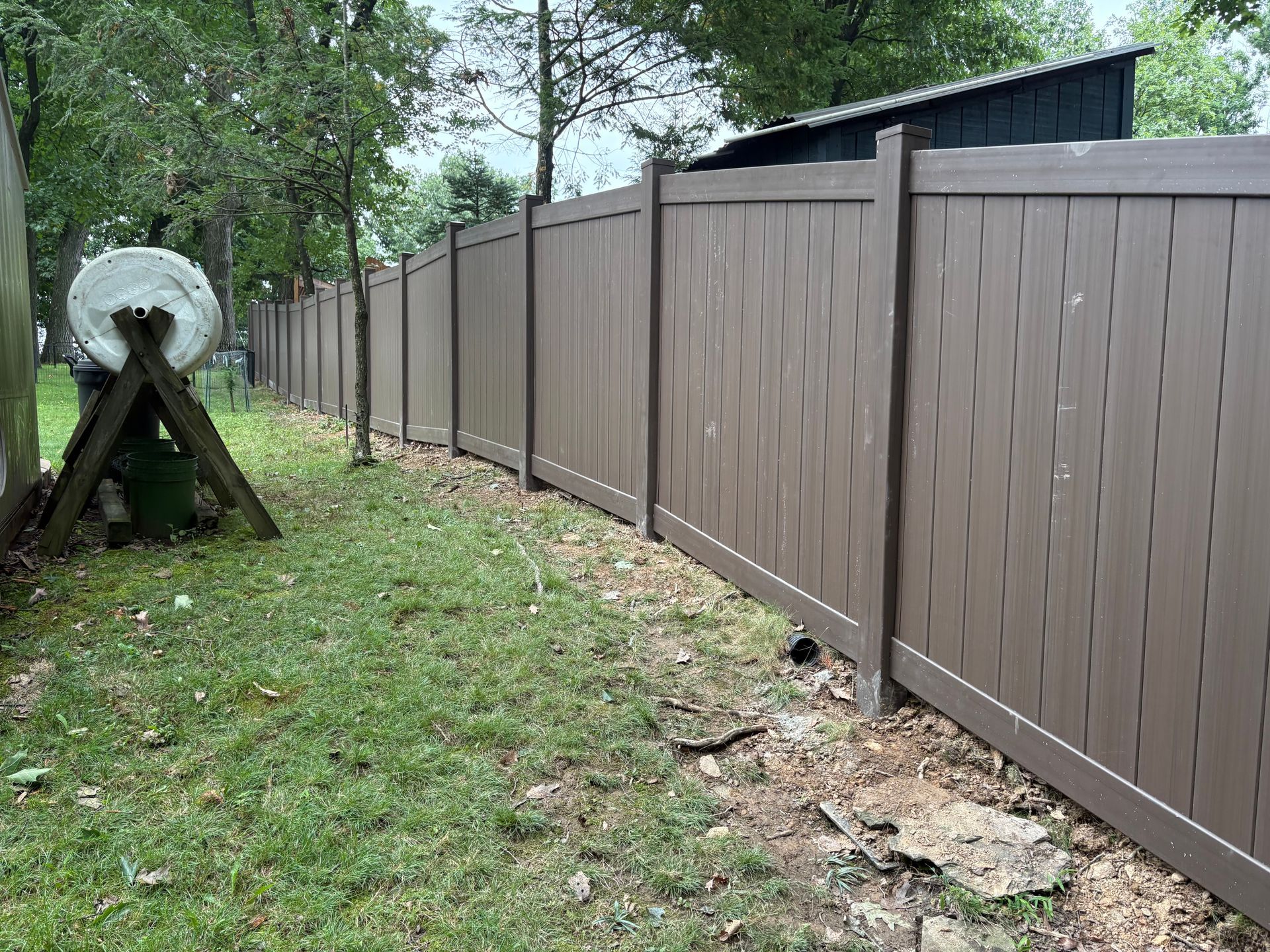 Brown privacy fence along a grassy yard with a large cable spool and trees nearby