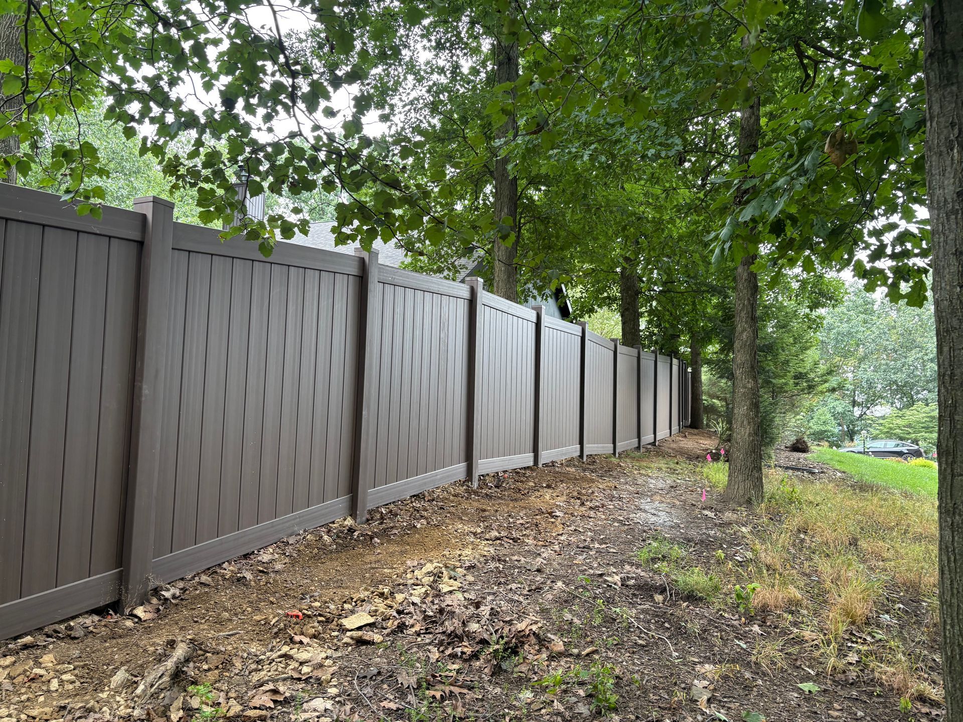 Brown wooden fence along a leafy wooded path beside a grassy area