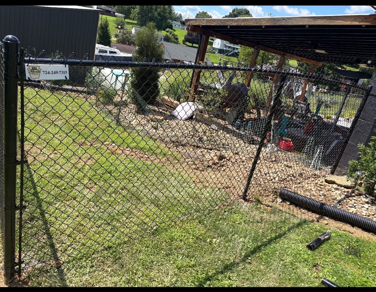 Chain-link fence beside a grassy yard with a shed and scattered debris under a partly cloudy sky