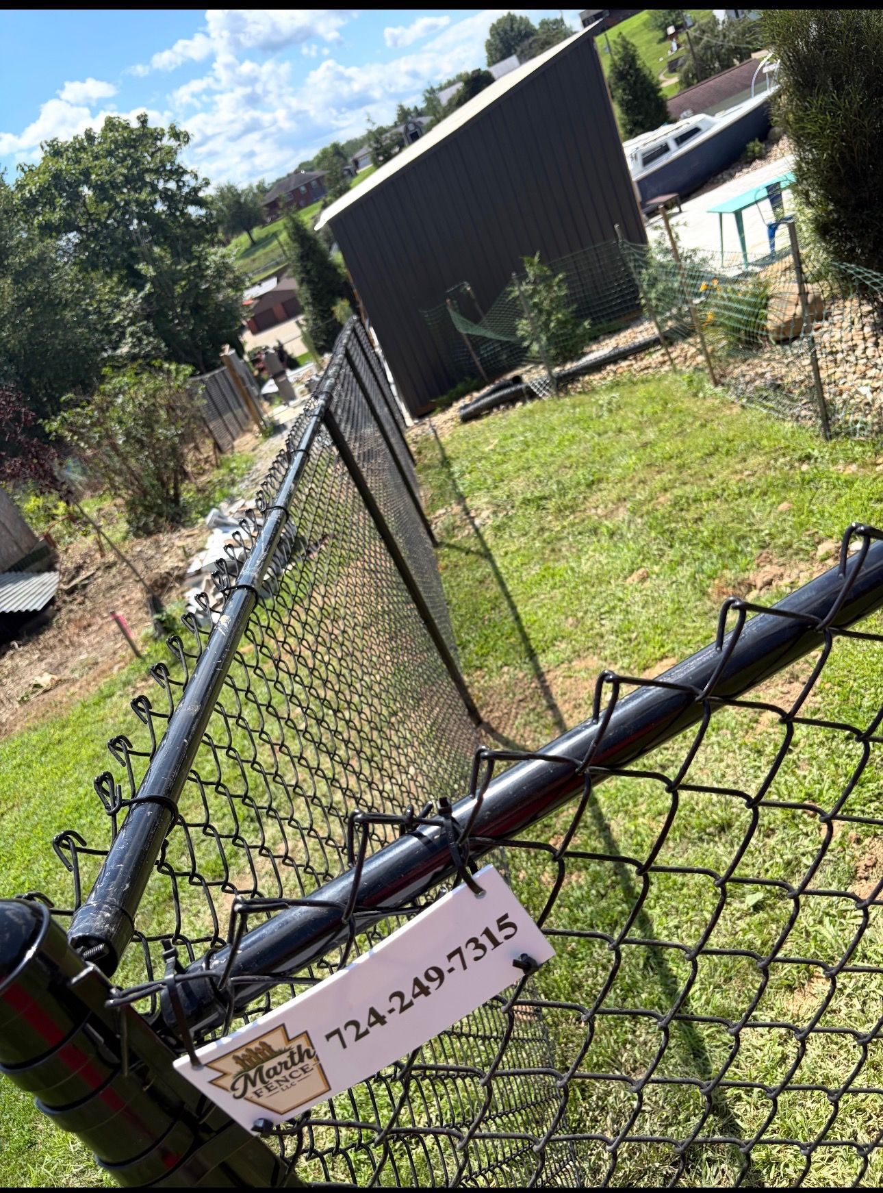 Tilted chain-link fence beside a grassy yard with a black shed and blue above-ground pool under a sunny sky