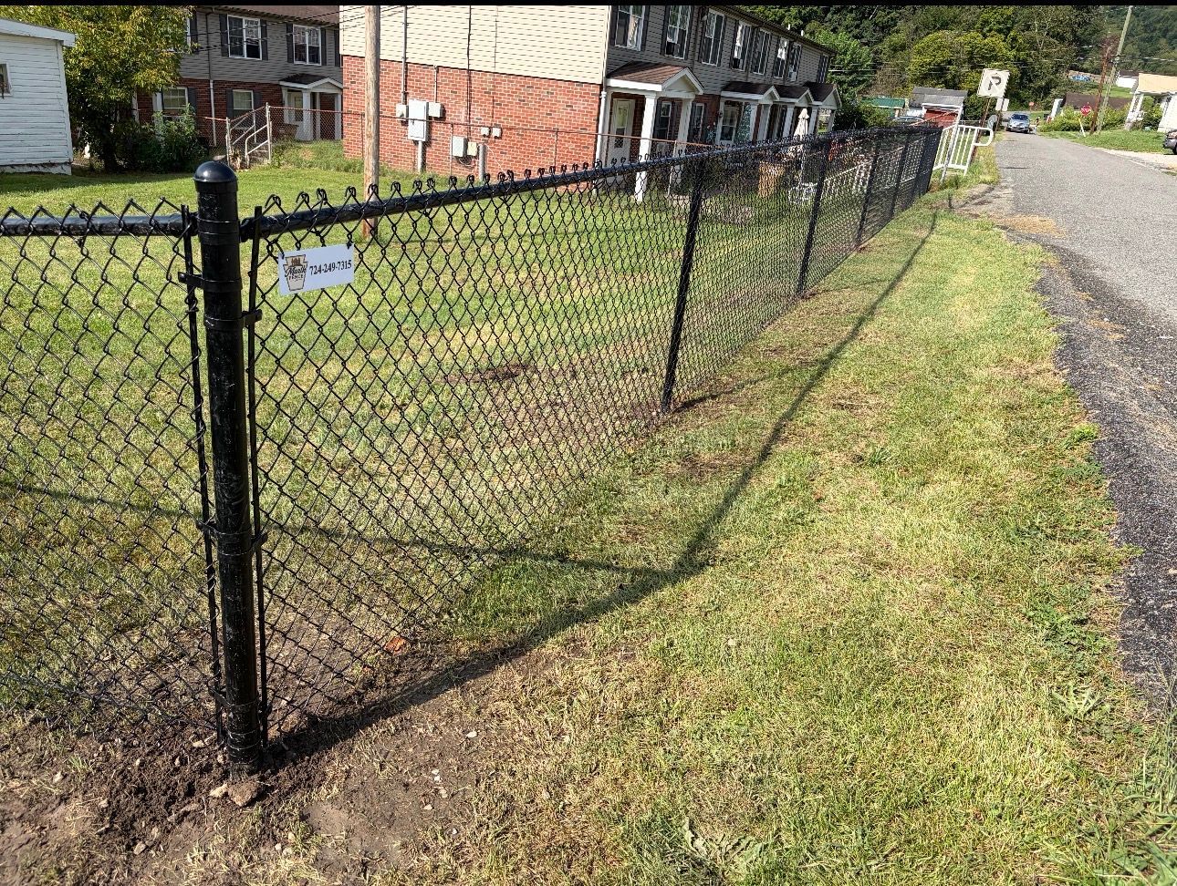 Black chain-link fence along a grassy roadside with houses in the background