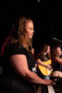 A woman is playing a piano on a stage while a man is playing a guitar.