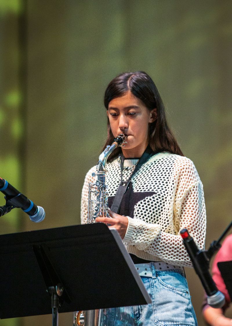 A young woman is playing a saxophone on a stage.