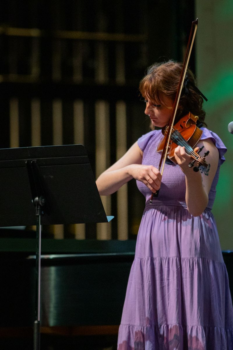 A woman in a purple dress is playing a violin on stage.