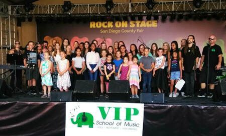 A group of children are standing on a stage in front of a sign that says vip school of music.