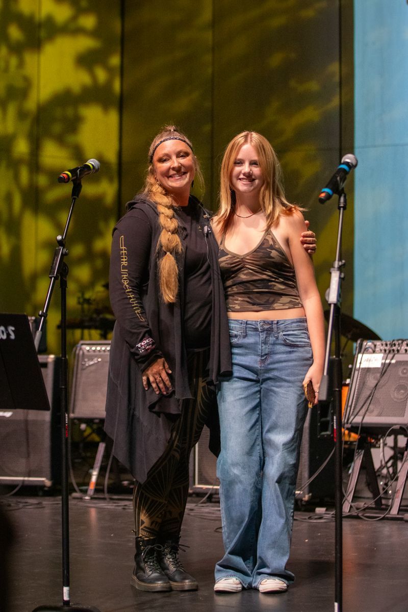 Two women are standing next to each other on a stage in front of a microphone.