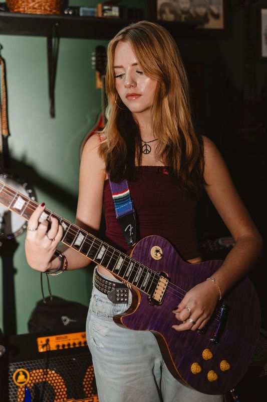 A young woman is playing a purple electric guitar in a room.