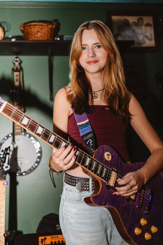 A young woman is holding a purple electric guitar.