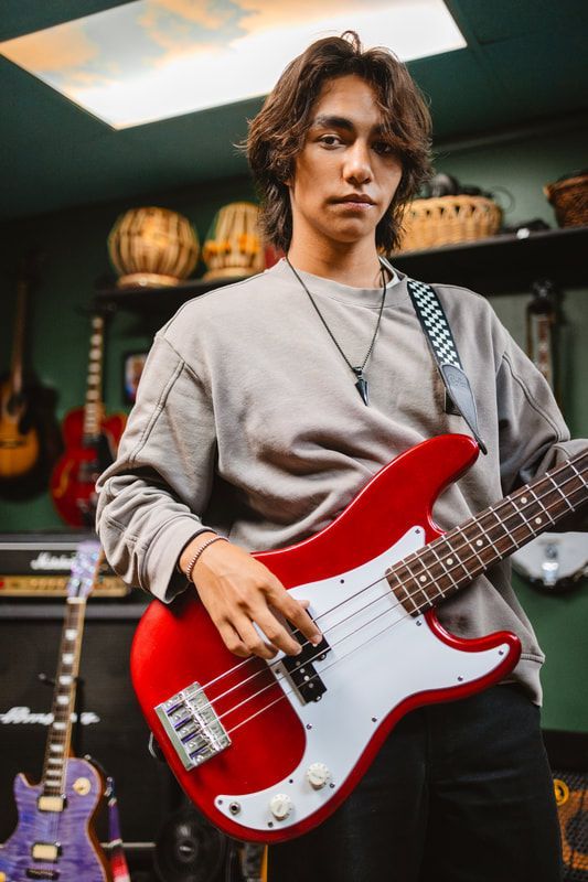 A young man is holding a red electric bass guitar in a room.