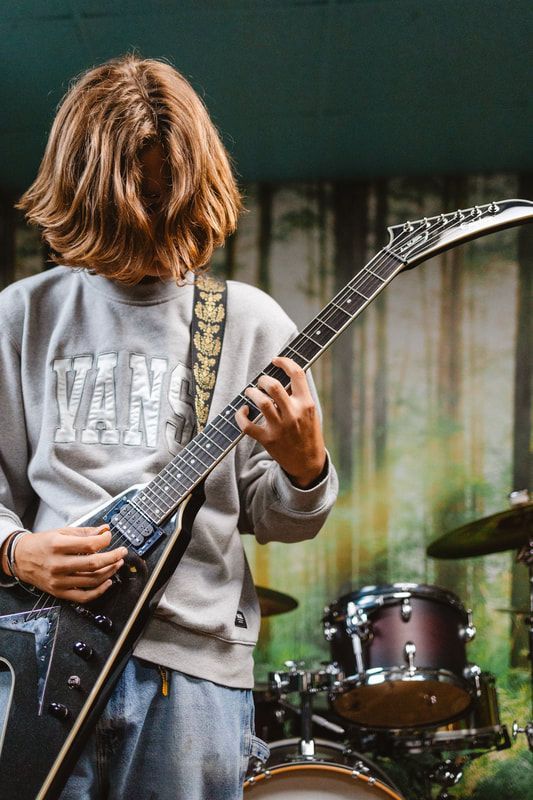 A young man is playing a guitar in front of a drum set.