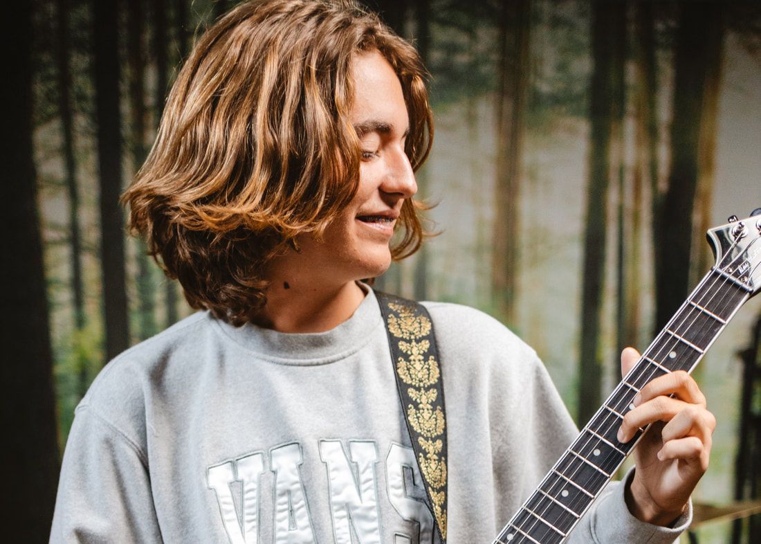 A young man is playing a guitar in front of a forest.