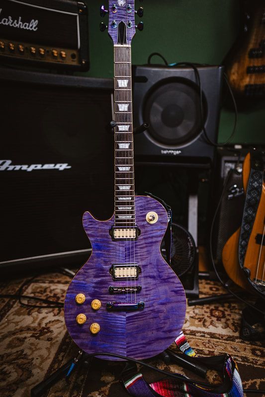 A purple electric guitar is sitting on a rug in front of a speaker.