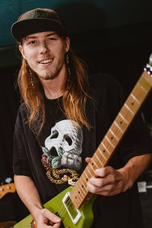 A young man with long hair is holding a green electric guitar.