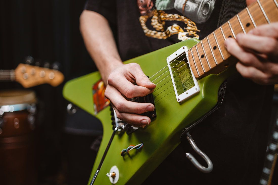 A man is playing a green electric guitar in a dark room.