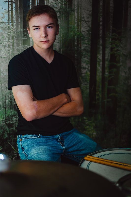 A young man is sitting in front of a drum set with his arms crossed.