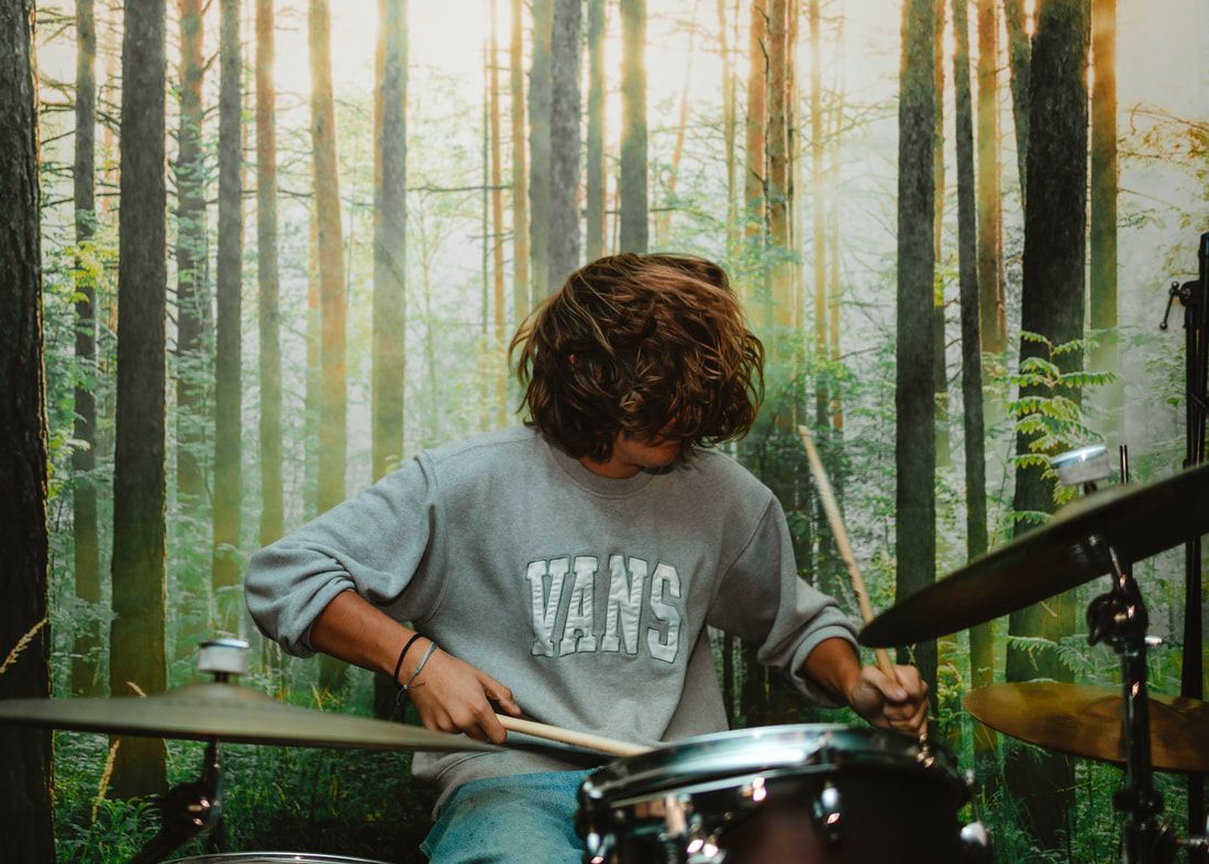 A young man is playing drums in front of a forest background.