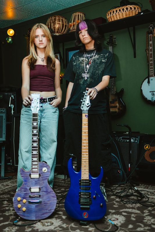 A man and a woman are standing next to each other holding guitars.