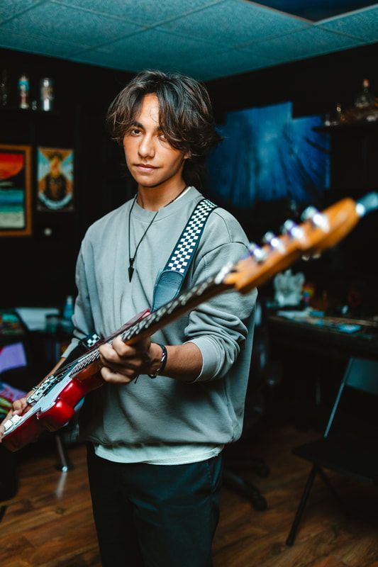 A young man is standing in a room holding a guitar.