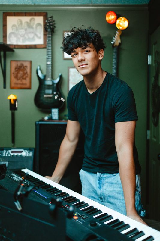 A young man in a black shirt is standing next to a piano keyboard.