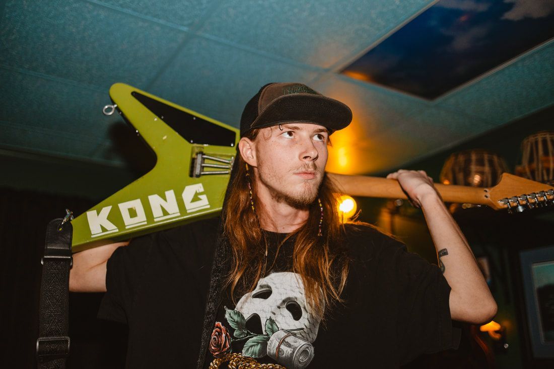 A man is holding a green kong guitar over his shoulder.