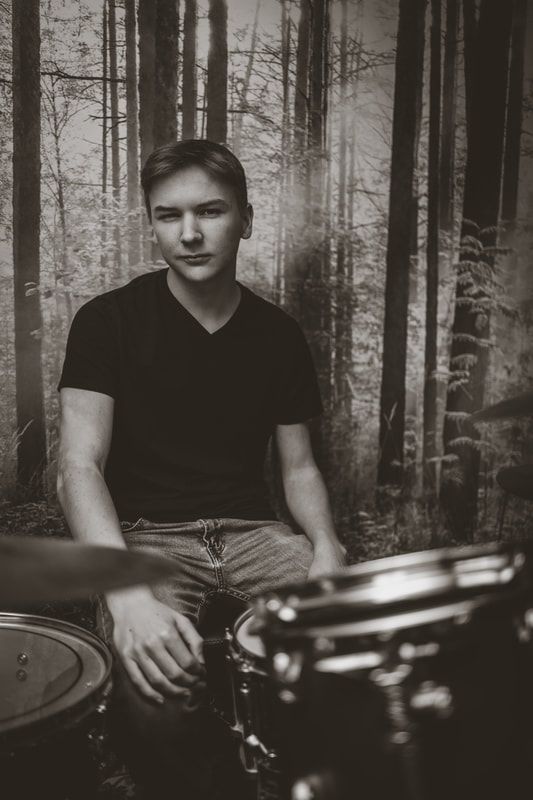 A young man is sitting in front of a drum set in a black and white photo.
