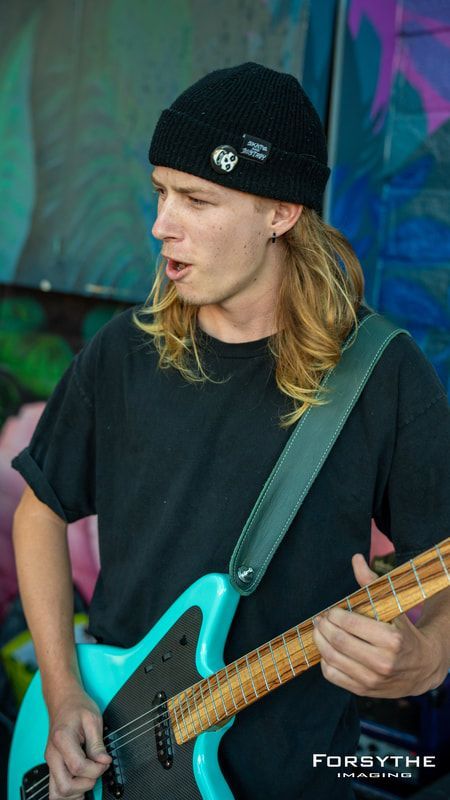 A young man is playing a blue guitar in front of a graffiti wall.