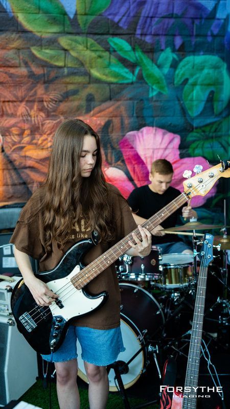 A woman is playing a guitar in front of a drum set.