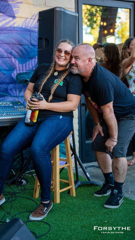 A man is kissing a woman on the cheek while she sits on a stool.