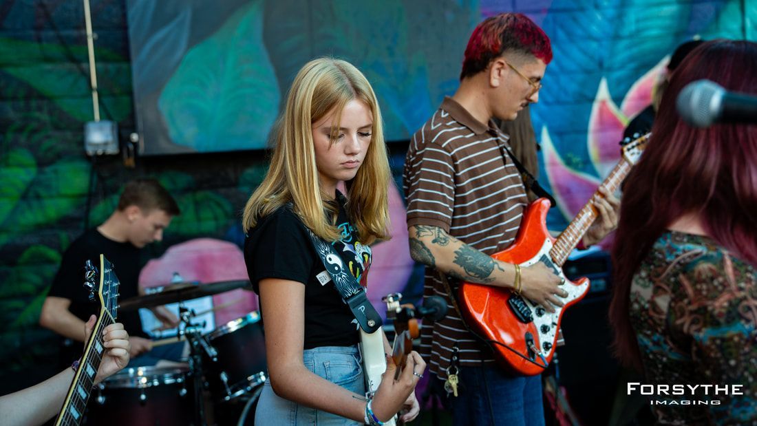 A girl is playing a guitar in a band