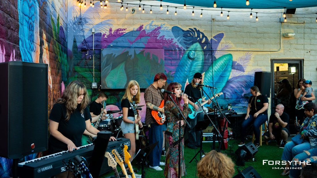 A group of people are playing instruments on a stage in front of a mural.