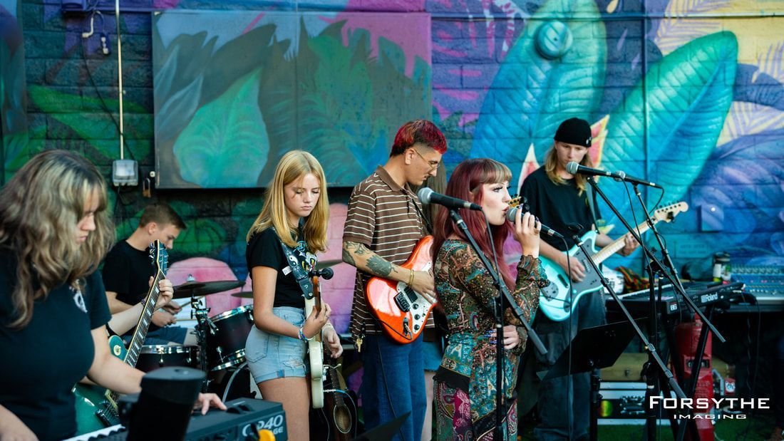 A group of people are playing instruments on a stage in front of a mural.