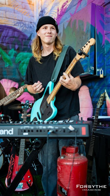 A man is playing a guitar and a keyboard in front of a graffiti wall.