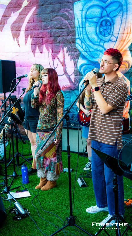 A group of people are singing into microphones in front of a mural.