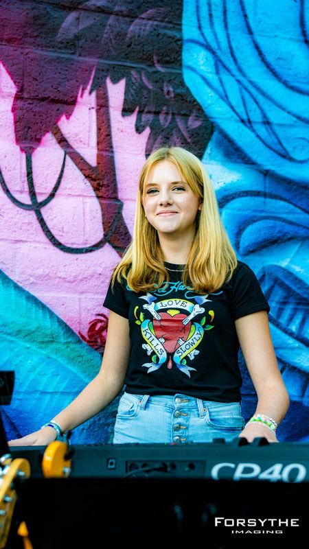 A young girl is playing a keyboard in front of a graffiti wall.