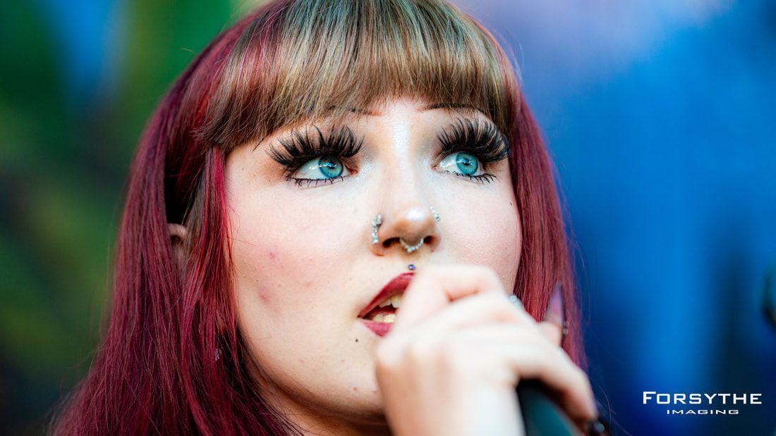 A woman with red hair and blue eyes is singing into a microphone.