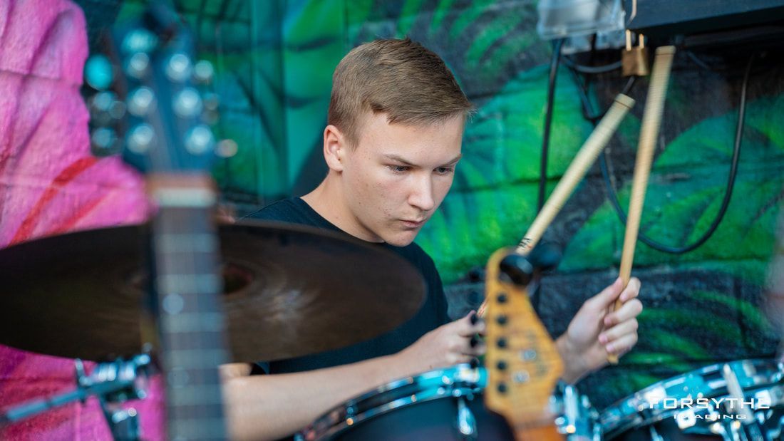 A young man is playing drums in front of a green wall.