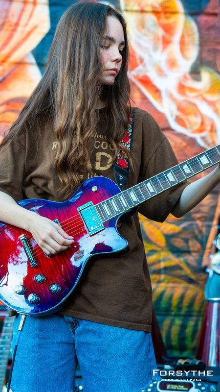 A woman is playing a guitar in front of a graffiti wall.