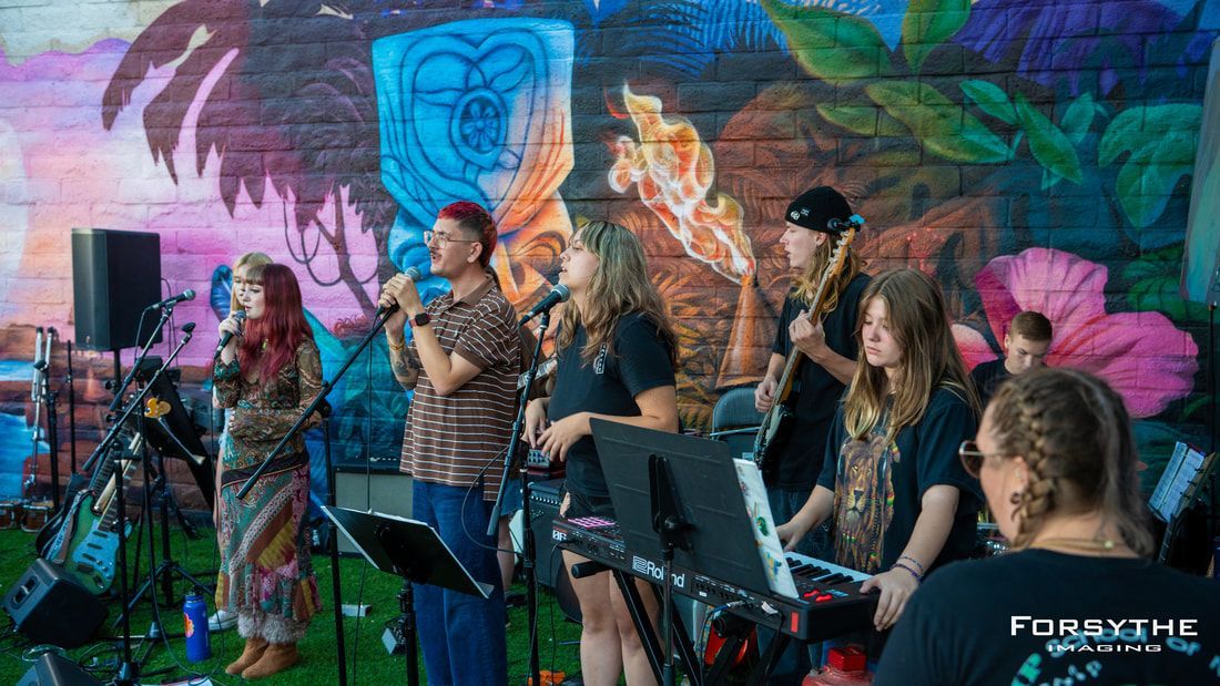 A group of people are singing and playing instruments in front of a mural.