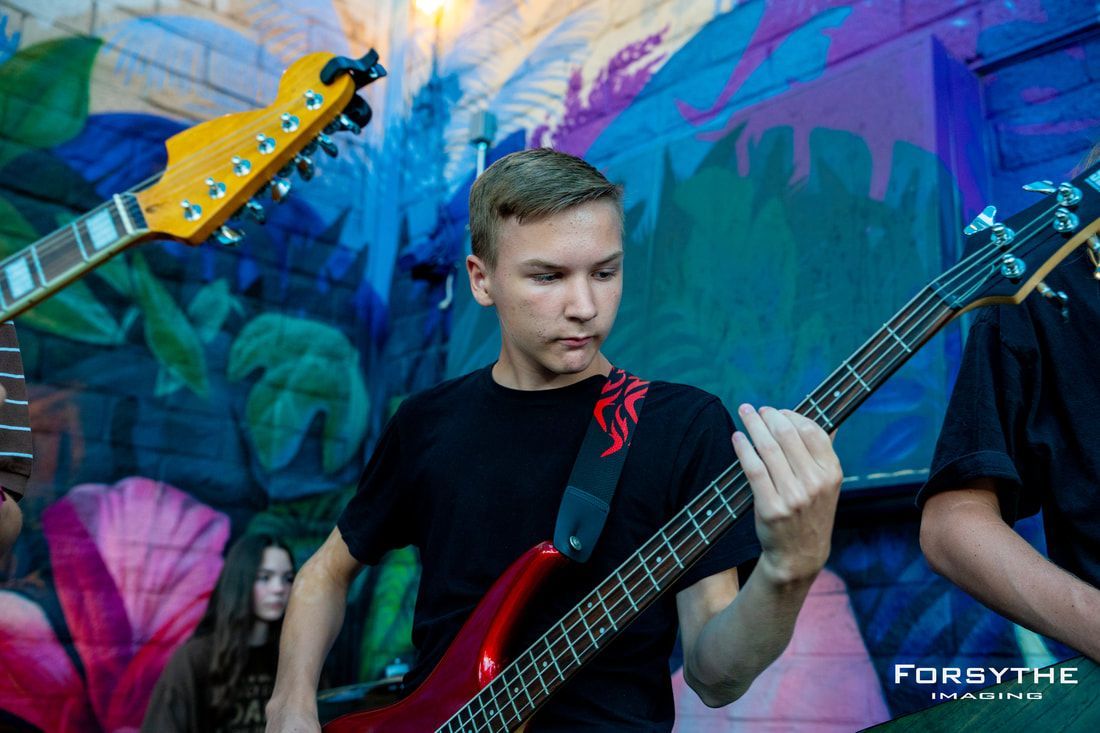 A young man is playing a red electric guitar in front of a mural.