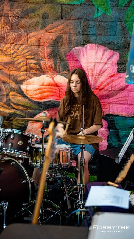 A woman is playing drums in front of a mural on a wall.
