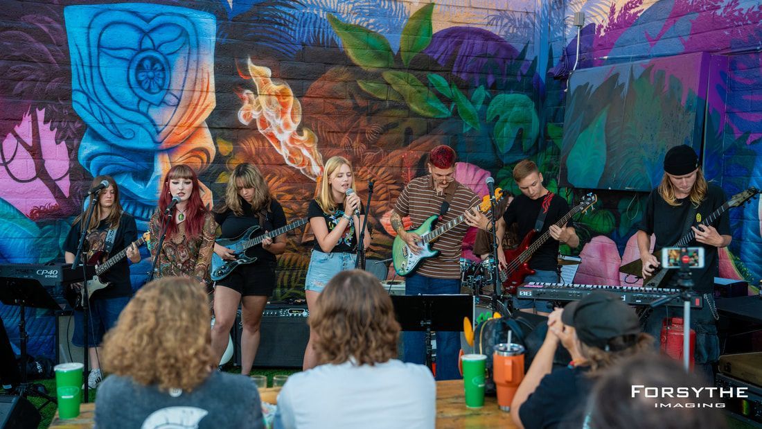A group of people are sitting in front of a mural watching a band perform on stage.