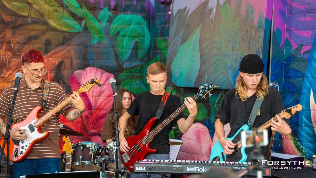 A group of people are playing guitars in front of a mural.