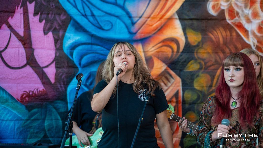 A woman is singing into a microphone in front of a graffiti wall.